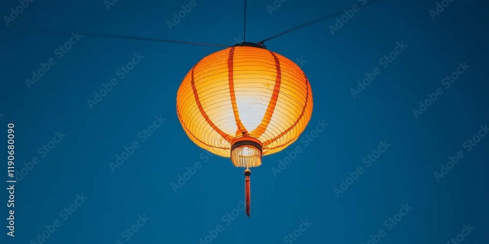 Obraz premium Beautifully Crafted Orange Lantern Hanging Against a Clear Blue Sky, Illuminating the Evening Atmosphere with Vibrant Tradition and Cultural Elegance