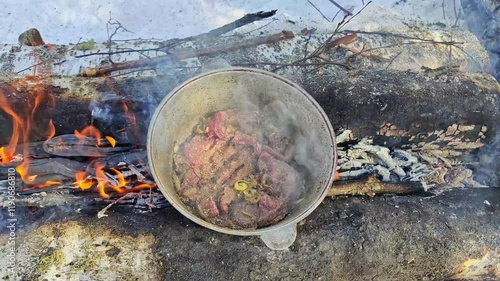 Cooking meat in a cauldron on a fire in winter. Frying meat close-up. Cooking outdoors in the winter wild forest