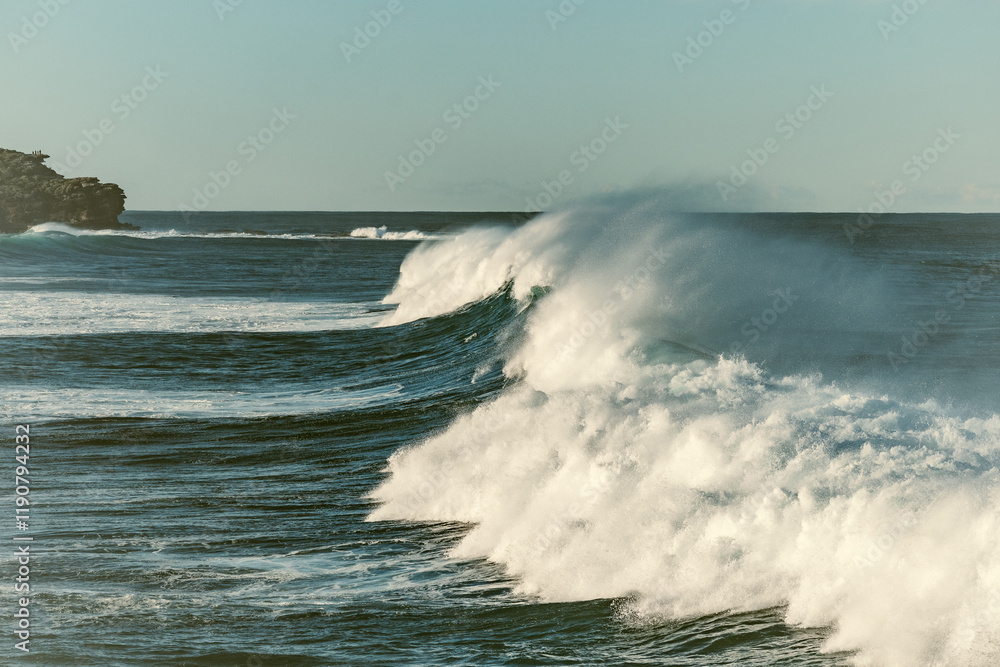 A series of powerful waves roll in, their crests breaking into white foam under the soft morning light. The dynamic motion of the water contrasts beautifully with the calm, open sea in the distance, w A series of powerful waves roll in, their crests breaking into white foam under the soft morning light. The dynamic motion of the water contrasts beautifully with the calm, open sea in the distance, w
