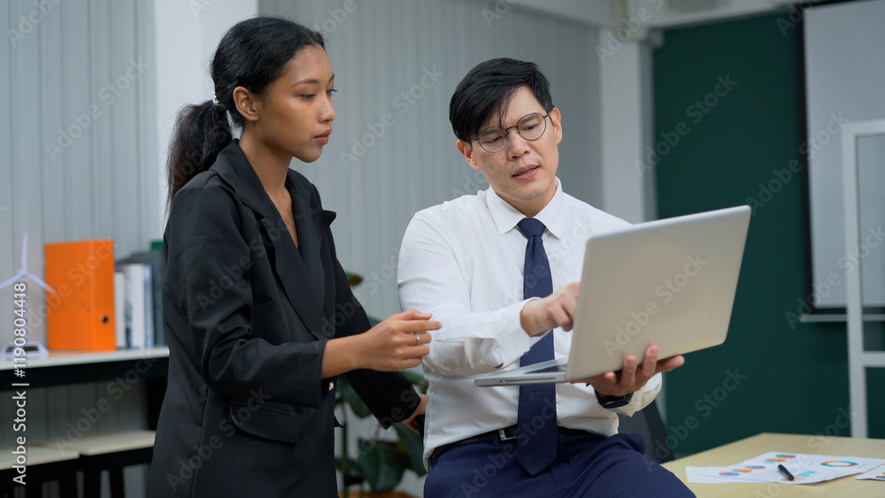 asian business man sitting on table holding laptop computer talking to worker woman standing in office . colleagues discussing project . brainstorming asian business man sitting on table holding laptop computer talking to worker woman standing in office . colleagues discussing project . brainstorming
