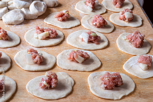 Homemade Dumplings. Small portions of minced meat are placed on circles of dough, dumplings will be made from them. Process of modeling pelmeni with minced meat filling on cutting board.   photo