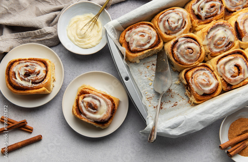 Tableau sur toile Freshly baked cinnamon rolls with cream cheese frosting and cinnamon sticks