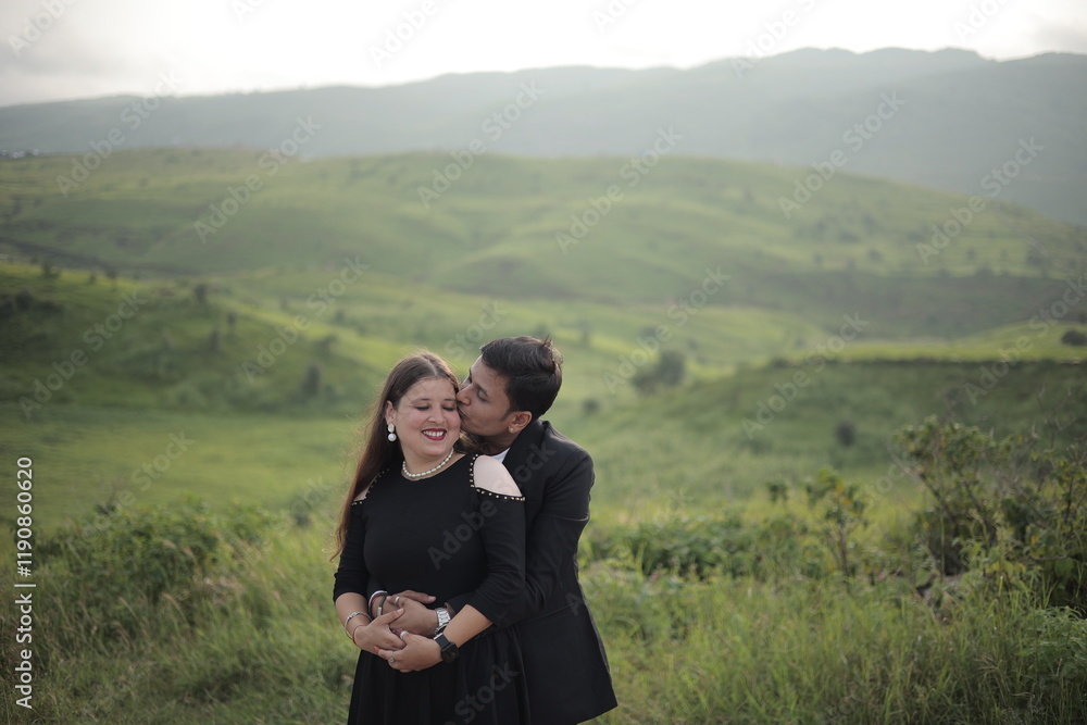 Loving young Indian couple in trendy clothes embracing against green mountains under sky Loving young Indian couple in trendy clothes embracing against green mountains under sky