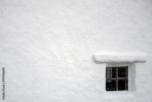A small window on the white plastered wall of the house. White wall of an old house with one window.