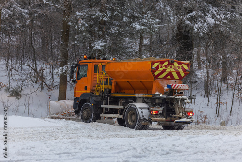 Snow plow and road salt spreader working on snowy road