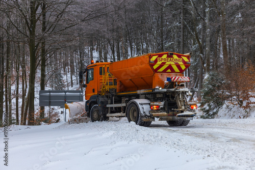 Snow plow and road salt spreader working on snowy road