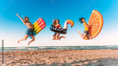 Three happy girls on jumping motion with inflatable mattresses at the beach for celebrating summer vacation - Friends women having fun outdoors on seaside holidays - Joy, carefree and party concept