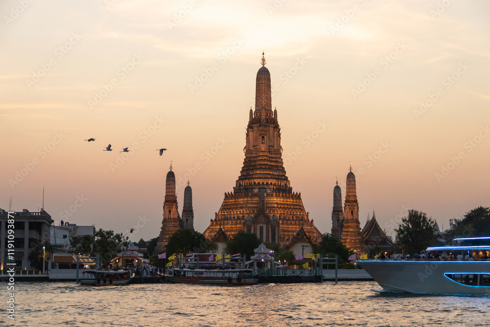 Fototapeta premium Wat Arun Ratchawararam Ratchawaramahawihan (Temple of Dawn) with a tourist on a cruise boat capturing a photo in a magical moment along the Chao Phraya river at twilight in Bangkok, Thailand.