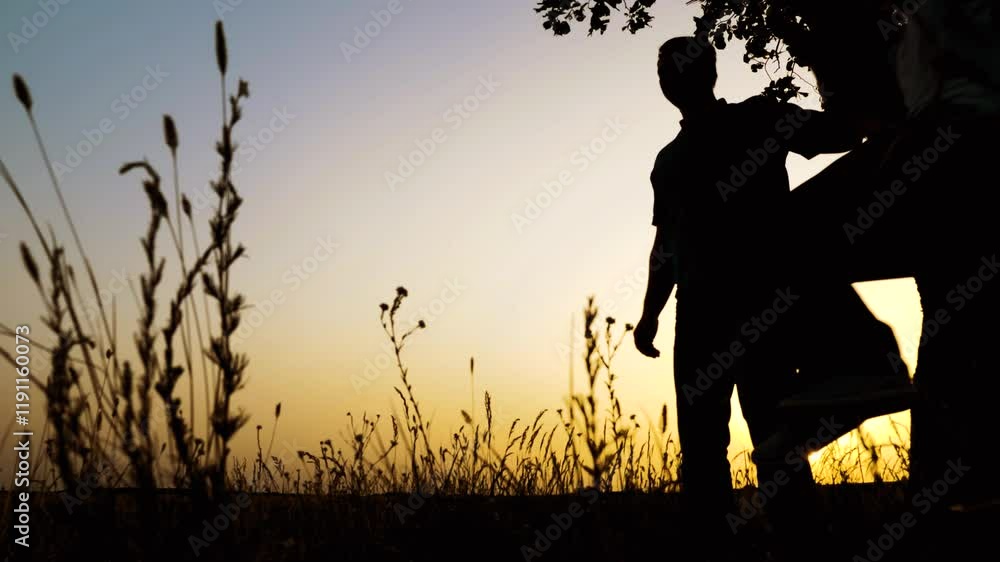 Loving father riding preteen son on swings dark silhouettes in country park against sunset sky. Little boy with father swinging silhouettes at twilight. Father and son play swings in evening field Loving father riding preteen son on swings dark silhouettes in country park against sunset sky. Little boy with father swinging silhouettes at twilight. Father and son play swings in evening field