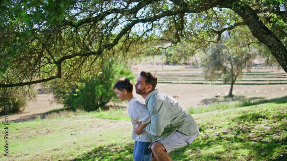 Smiling dad carrying child on grassy lawn. Joyful father holding son at garden Smiling dad carrying child on grassy lawn. Joyful father holding son at garden