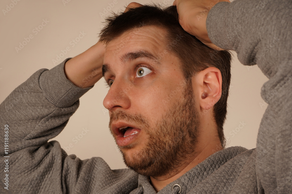 Obraz premium Holding his hair in his fist, the man shows clear signs of tension or stress. His face reflects a moment of suffering. The pose creates an irresistible feeling of mental tension.