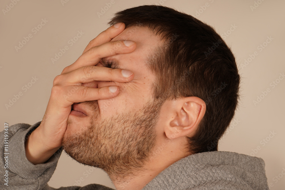 Fototapeta premium The man places his palm on his face, performing a facepalm gesture. This classic gesture expresses frustration, disbelief, or embarrassment. It s a universal sign of exasperation or regret.