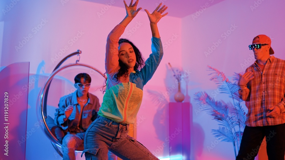 Fototapeta premium Attractive happy dancer looking at camera while smart woman moving at rhyme with neon light. Professional hispanic performer break dancing while wearing colorful cloth with diverse friend. Regalement.