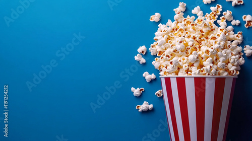 delicious buttery popcorn spilling from a red and white striped cinema bucket on a blue background for a movie night snack photography