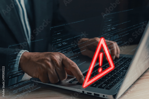 A professional uses a laptop displaying a glowing red warning triangle with an exclamation mark, symbolizing caution and cybersecurity threats in a digital environment filled with code. photo