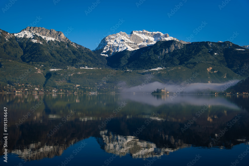Obraz premium Wide Shot of Lake Annecy Reflecting Mountains and Château de Duingt Surrounded by Fog, France.