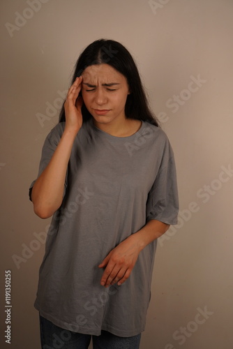 The scene focuses on the need for pain management and alleviation. The woman touches her temple with one hand, signaling the agony of a bad headache. Her posture emphasizes the discomfort. photo