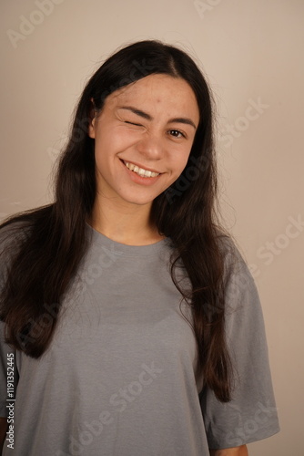 This candid moment radiates positivity and charm. The girl closes one eye and slightly opens her lips, revealing her teeth in a bright smile. Her playful expression shows joy and confidence. photo