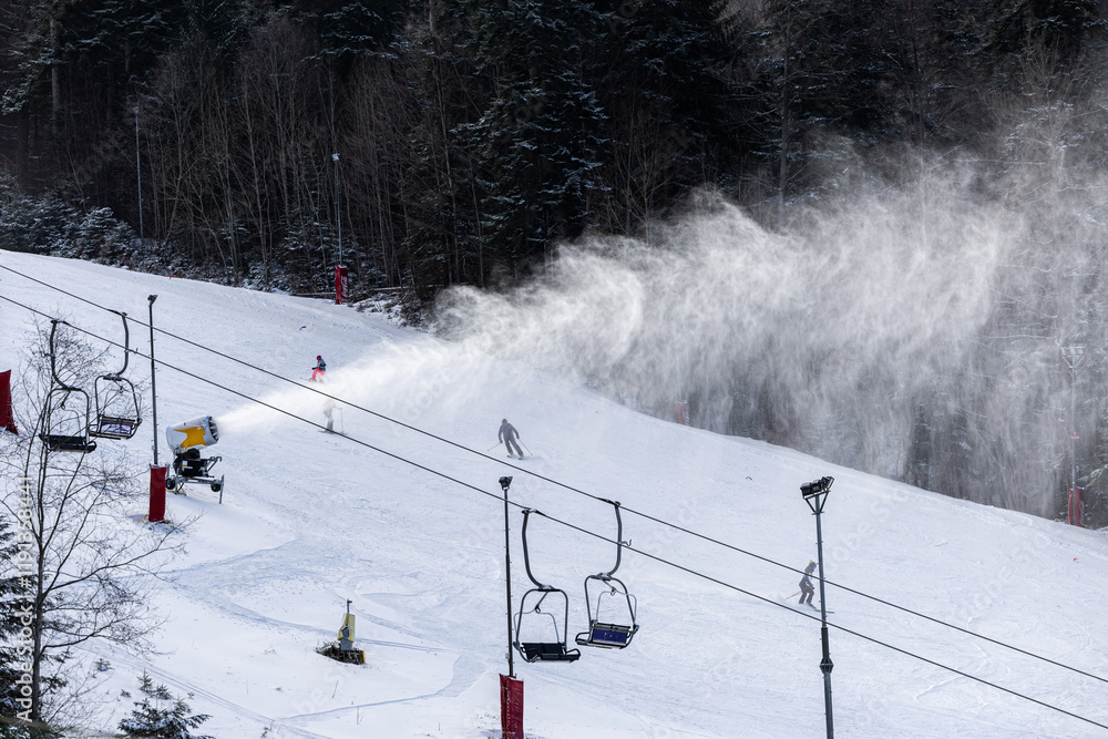 Snow making in a mountain resort. Beautiful view with snow cannons powered on to create snow from water and to keep the slopes available for tourists.