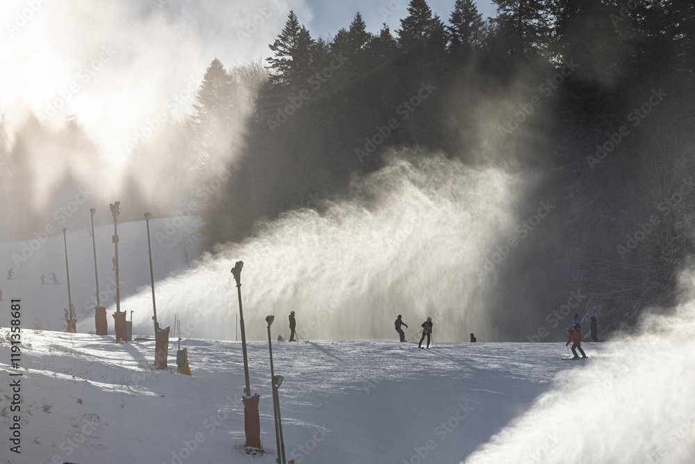 Winter ski resort. Beautiful view with clouds of snow created by the snow cannon machine. Tourist skiing on slopes. Winter sports.