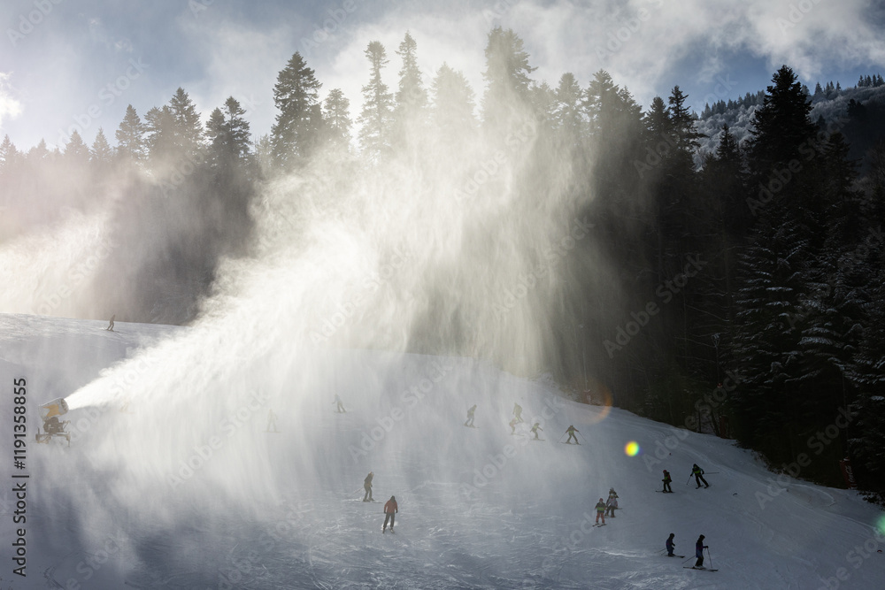 Winter ski resort. Beautiful view with clouds of snow created by the snow cannon machine. Tourist skiing on slopes. Winter sports.
