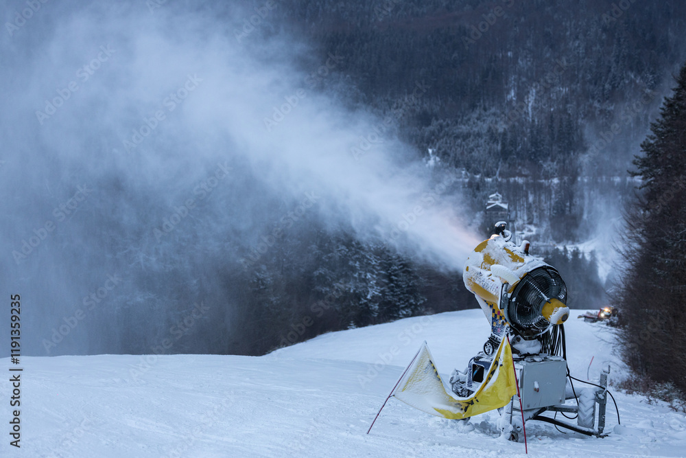 Snow cannon in the evening. Snow making machine on ski slope in the evening to prepare the mountain ski resort for the next day. Winter sports industry.