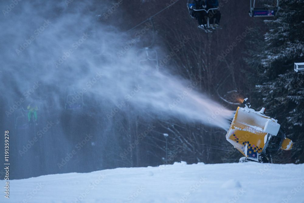 Snow cannon in the evening. Snow making machine on ski slope in the evening to prepare the mountain ski resort for the next day. Winter sports industry.
