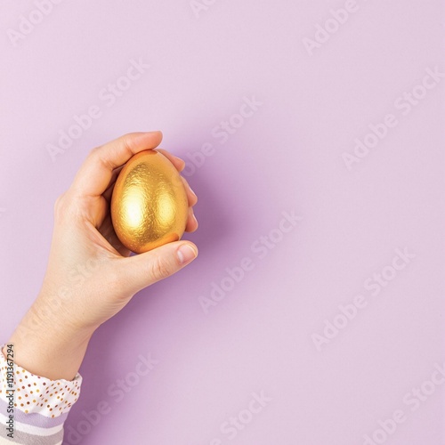 Small Child Hand Holding Golden Easter Egg on Light Purple photo