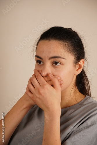 The hands symbolize restraint and control. A woman covers her mouth with her hands as if to hold back a scream. This gesture conveys a struggle to contain emotions or stifle a reaction. photo