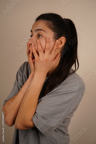 Wallpaper Mural The interesting facial expression conveys a moment of surprise. The focus is on her emotions. A young woman holds her hands over her face, her eyes wide open and her mouth open in genuine surprise. Torontodigital.ca