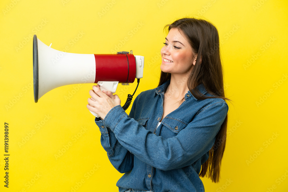 Young caucasian woman isolated on yellow background shouting through a megaphone to announce something Young caucasian woman isolated on yellow background shouting through a megaphone to announce something