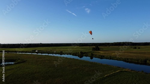 View of a Paraglider Flying at Sunset Over a River and Scenic Green Fields Drone Aerial 4K Slow Motion