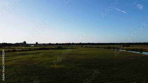 View of a Paraglider Flying at Sunset Over a River and Scenic Green Fields Drone Aerial 4K Slow Motion