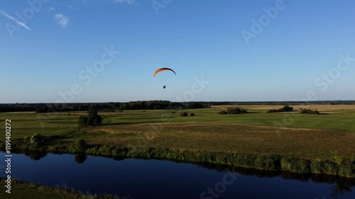 View of a Paraglider Flying at Sunset Over a River and Scenic Green Fields Drone Aerial 4K Slow Motion