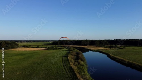 View of a Paraglider Flying at Sunset Over a River and Scenic Green Fields Drone Aerial 4K Slow Motion