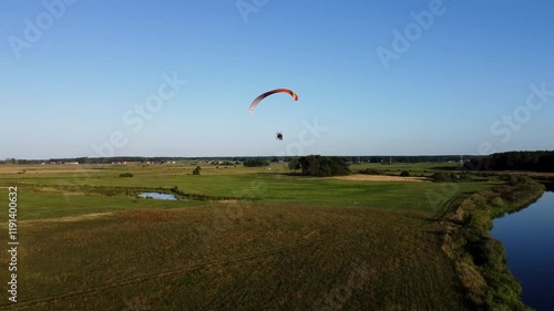 View of a Paraglider Flying at Sunset Over a River and Scenic Green Fields Drone Aerial 4K Slow Motion