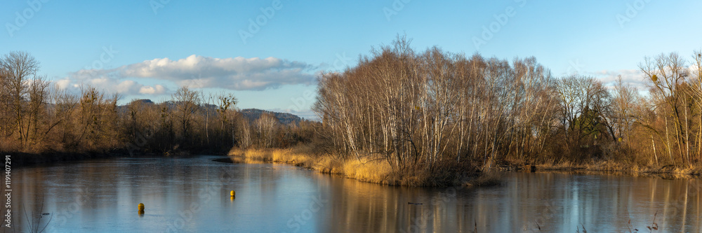 Fototapeta premium Panorama with Sunset on the Old Rhine with illuminated reeds and bushes on the shore of the lake, sun star and sunset red, impressive colors between autumn and winter