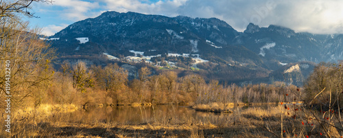 Panorama with Sunset on the Old Rhine with illuminated reeds and bushes on the shore of the lake, sun star and sunset red, impressive colors between autumn and winter, snowy mountains in background photo