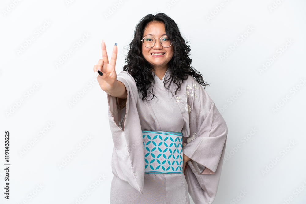 Young asian woman wearing kimono isolated on white background smiling and showing victory sign Young asian woman wearing kimono isolated on white background smiling and showing victory sign