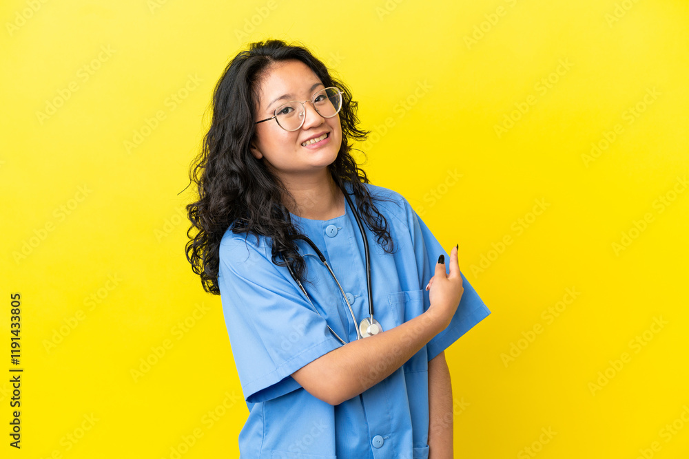 Young surgeon doctor asian woman isolated on yellow background pointing back Young surgeon doctor asian woman isolated on yellow background pointing back