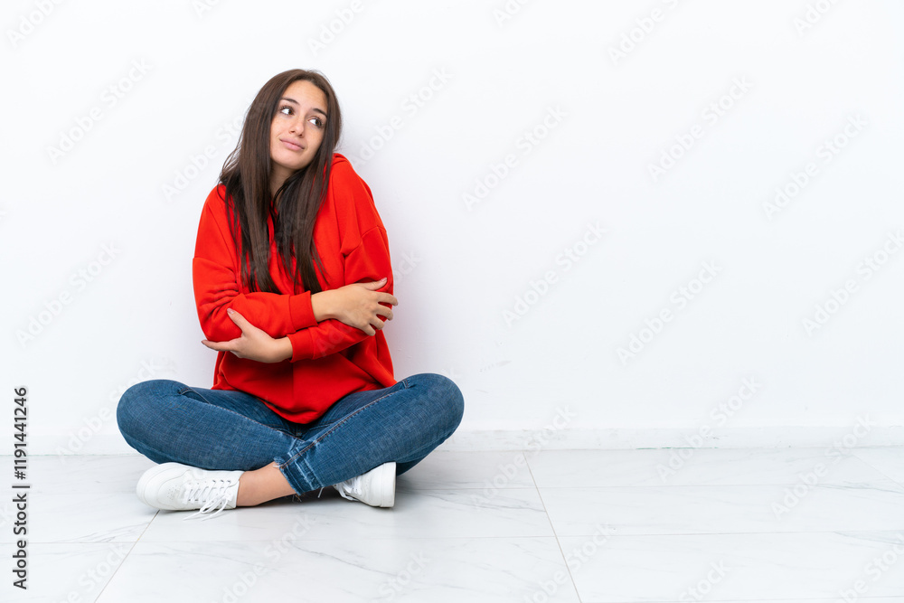 Young Ukrainian woman sitting on the floor isolated on white background making doubts gesture while lifting the shoulders Young Ukrainian woman sitting on the floor isolated on white background making doubts gesture while lifting the shoulders