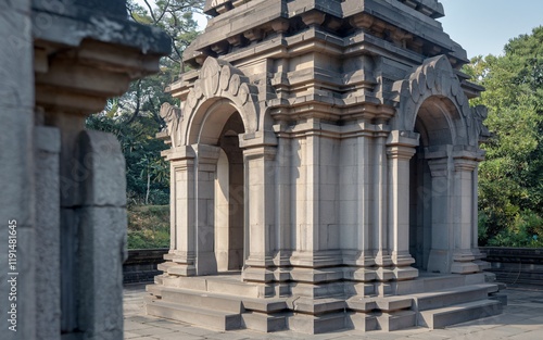 Ancient stone structure with intricate carvings and arched doorways, nestled in a serene, leafy setting.