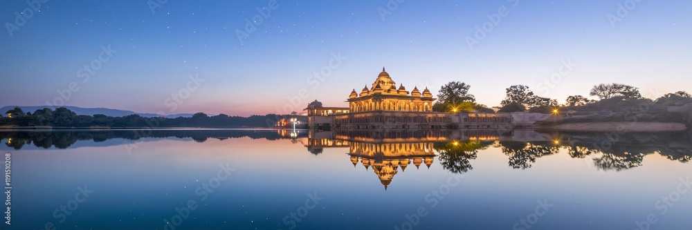 Fototapeta premium Illuminated temple reflected in calm lake at dawn.