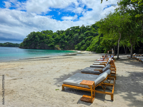 Blanca Beach and the blue waters of Culebra Bay, lush green trees, lounge chairs on the sandy beach, blue sky and clouds in Liberia Guanacaste Costa Rica
