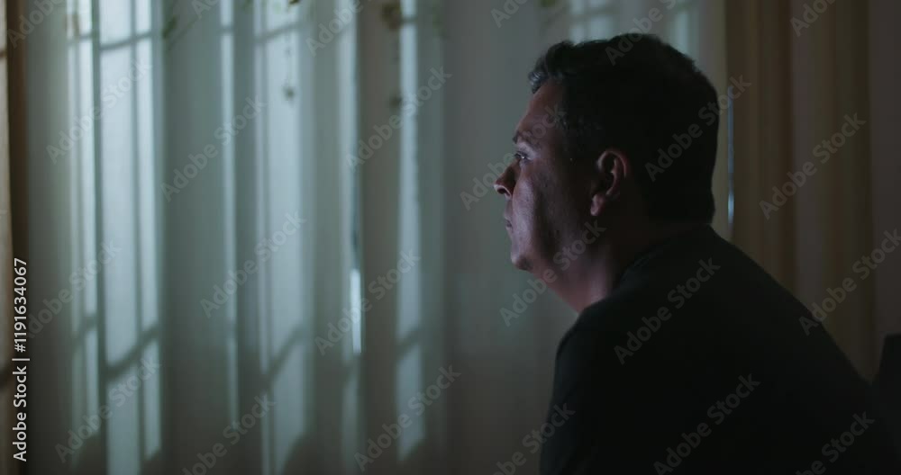 Man leaning forward paying attention to TV screen content with focused concentration, curtains in background, intense and engaging moment in cozy indoor setting Man leaning forward paying attention to TV screen content with focused concentration, curtains in background, intense and engaging moment in cozy indoor setting