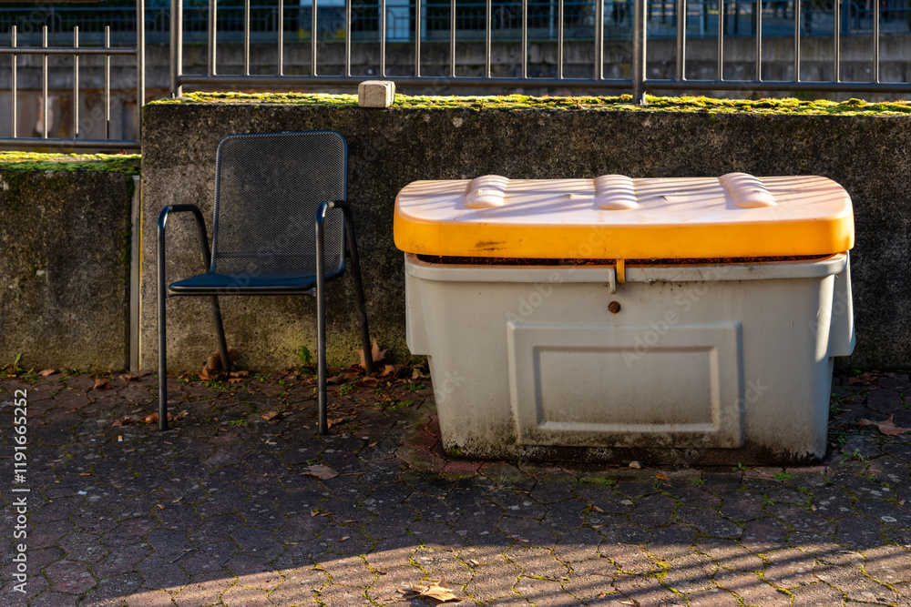 Fototapeta premium Unused chair beside a storage container on a sunny day in an urban environment
