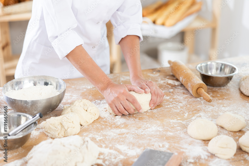 Fototapeta premium Female baker in uniform kneading raw dough close-up