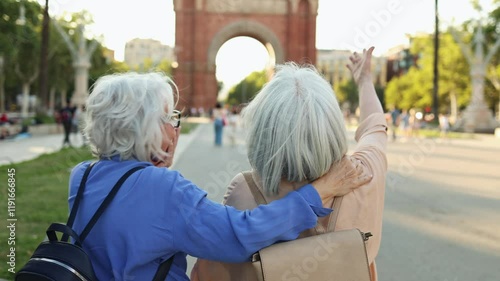 Senior women exploring barcelona, visiting arc de triomf. Senior women travelers pointing at arc de triomf, enjoying vibrant barcelona sightseeing adventure together under sunny skies