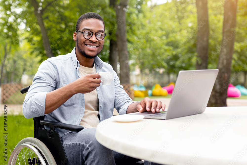 Happy handicapped black man in wheelchair using laptop for online job at cafe in city park, having business meeting on web, outdoors. African American disabled freelancer guy working on remote project Happy handicapped black man in wheelchair using laptop for online job at cafe in city park, having business meeting on web, outdoors. African American disabled freelancer guy working on remote project