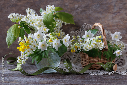 Still life with spring white and yellow flowers, anemones, primroses and blooming bird cherry in a vase and basket on an old wooden table